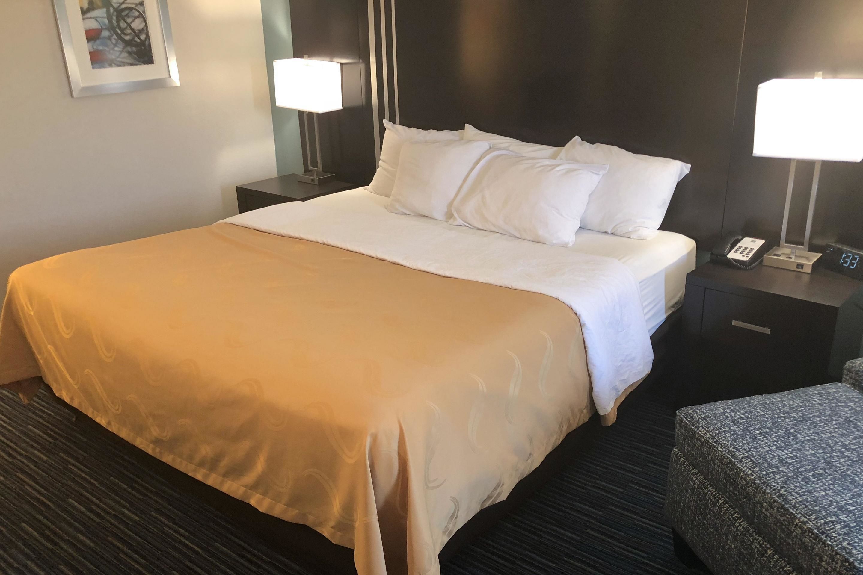 A hotel room with a large bed, two bedside tables with lamps, a telephone, and a digital clock.