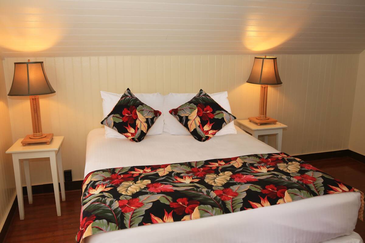A bed with a floral bedspread, two white pillows, and two bedside lamps on white nightstands.