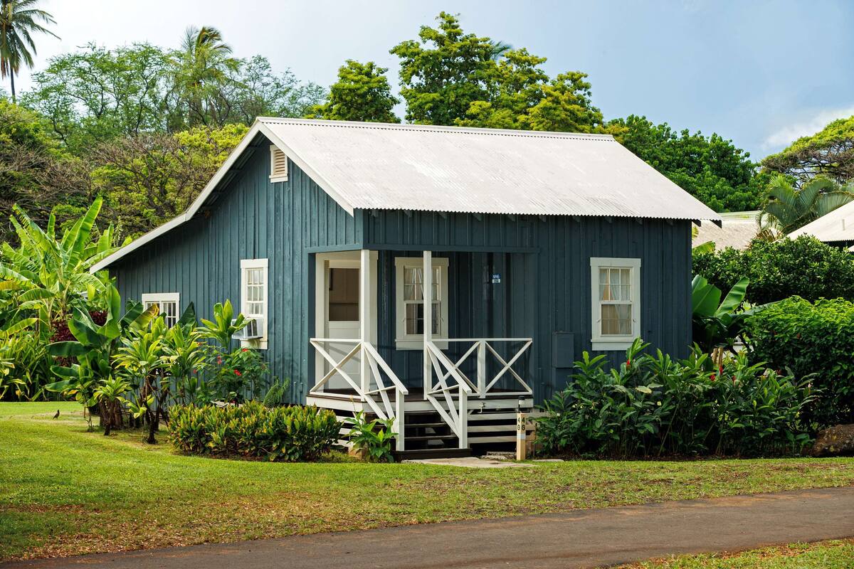 A small, single-story building with a porch and steps, surrounded by lush greenery.