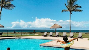 A swimming pool with clear blue water, surrounded by lounge chairs and palm trees, with a view of the ocean in the background. - Waimea Plantation Cottages, a Coast Resort (Waimea)