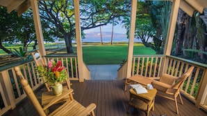 A wooden deck with wicker furniture, a potted plant, and a view of a grassy area and water. - Waimea Plantation Cottages, a Coast Resort (Waimea)