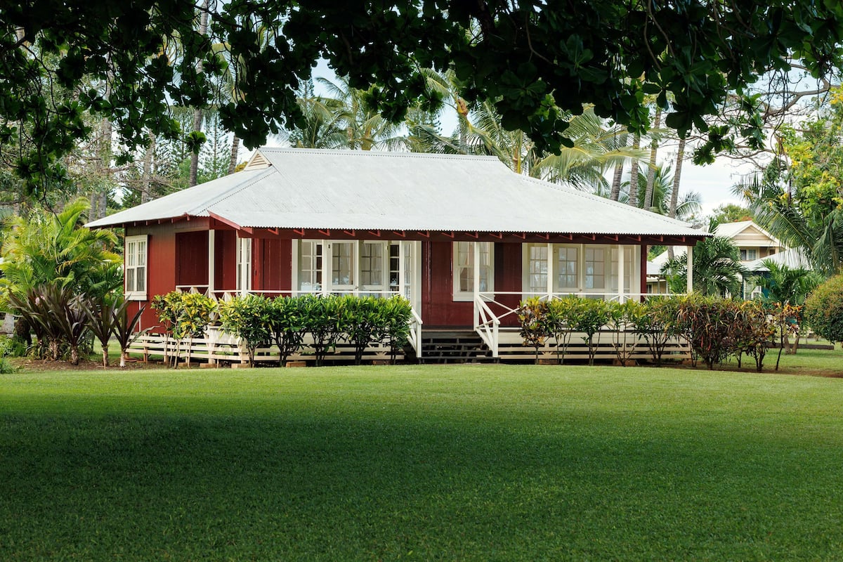A red building with a white porch and steps, surrounded by green grass and trees.
