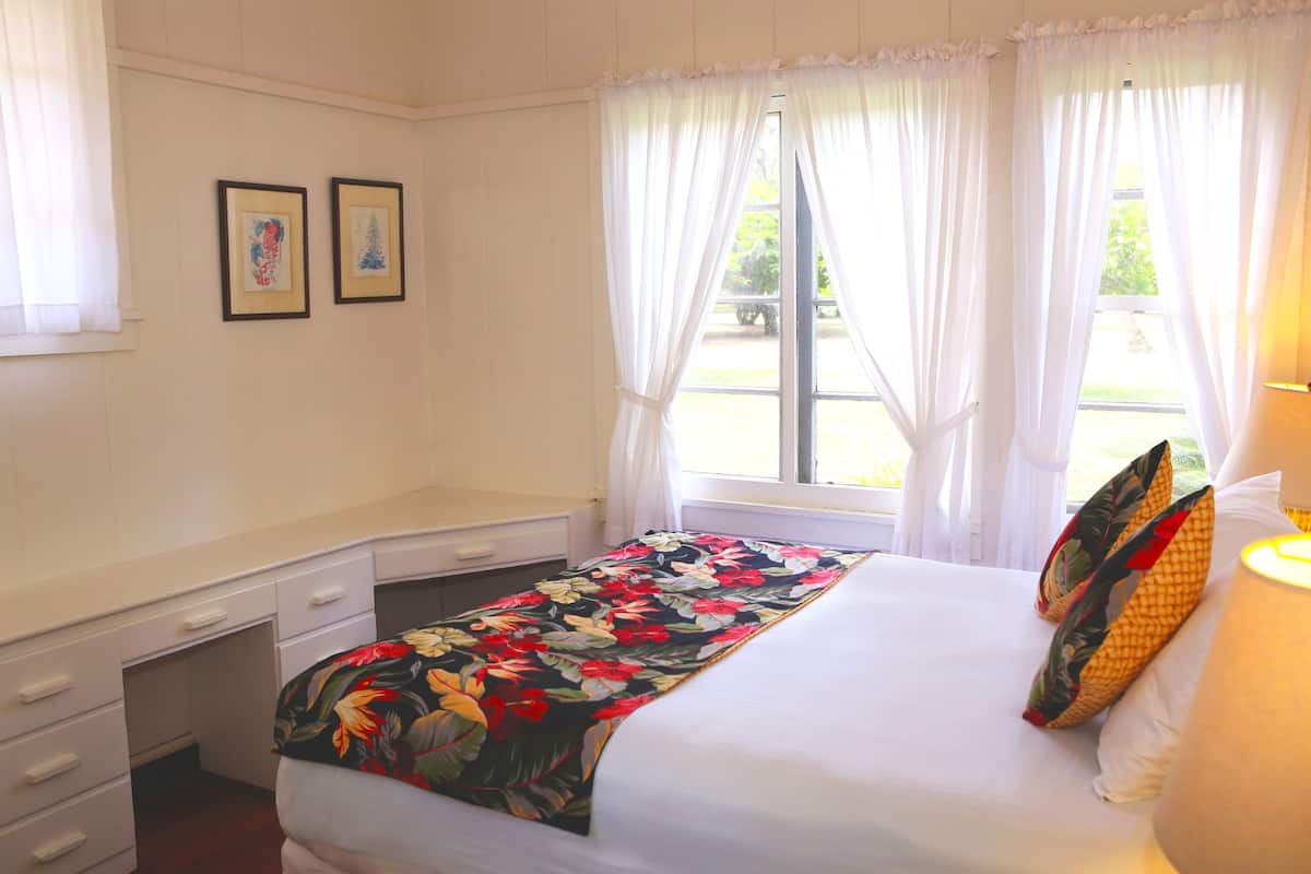 A hotel room with a bed, a desk, and two framed pictures on the wall.