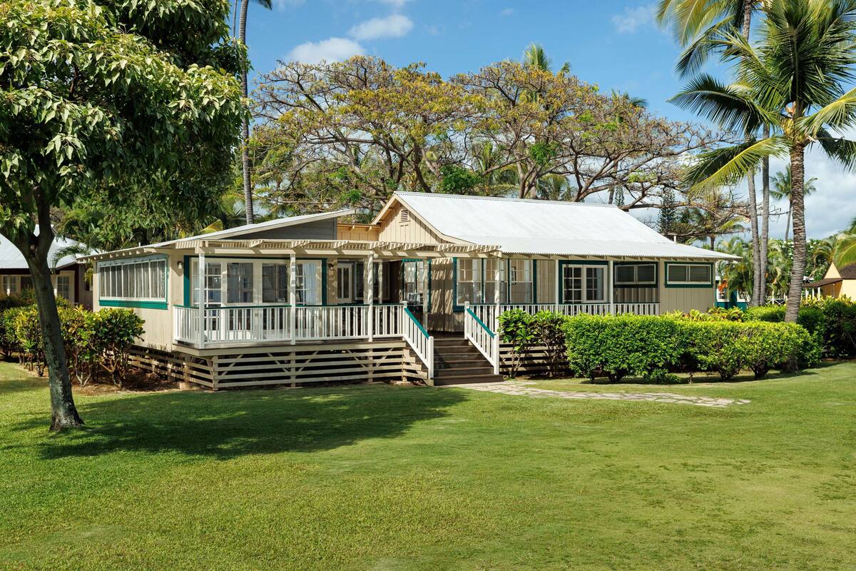 A two-story house with a porch, surrounded by well-maintained lawns and palm trees.