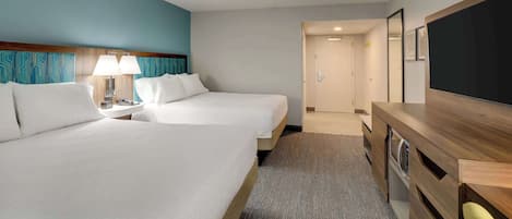 A hotel room with two beds, a desk, a TV, and a bathroom visible through an open door.
