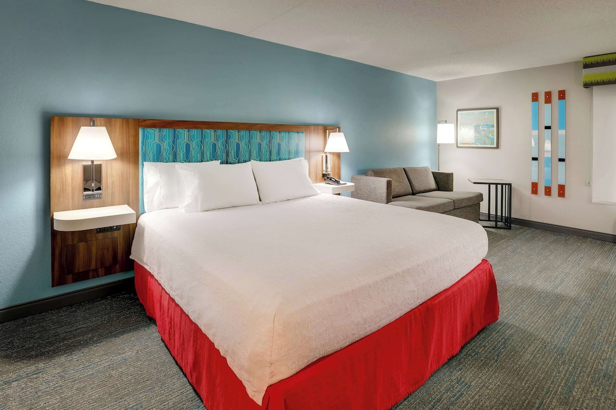 A hotel room with a large bed, two bedside tables, a nightstand, a sofa, and a small table with a lamp.