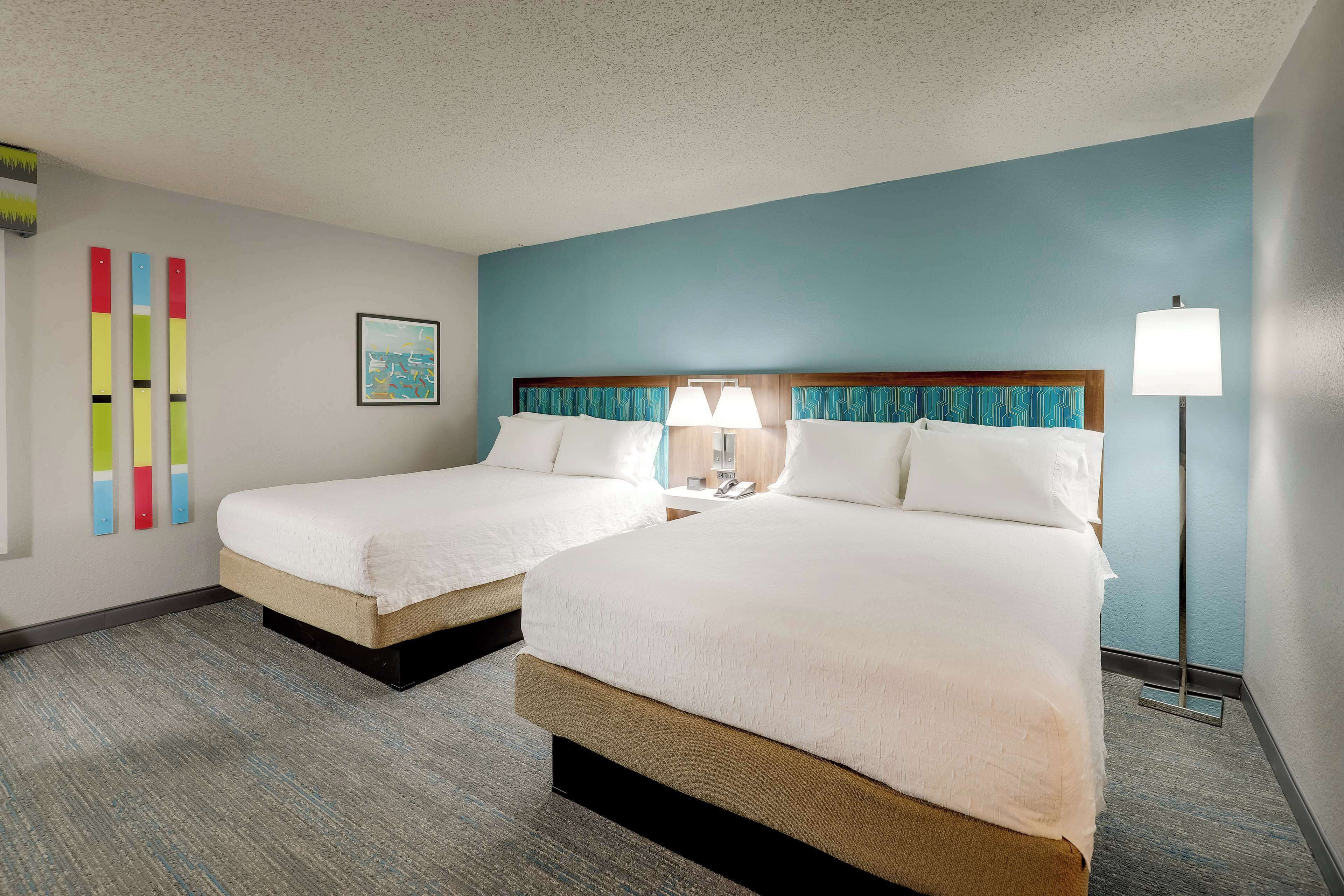 A hotel room with two beds, a blue accent wall, and a floor lamp.
