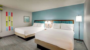 A hotel room with two beds, a blue accent wall, and a floor lamp.