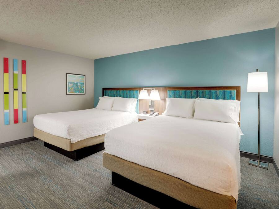 A hotel room with two beds, a blue accent wall, and a floor lamp.