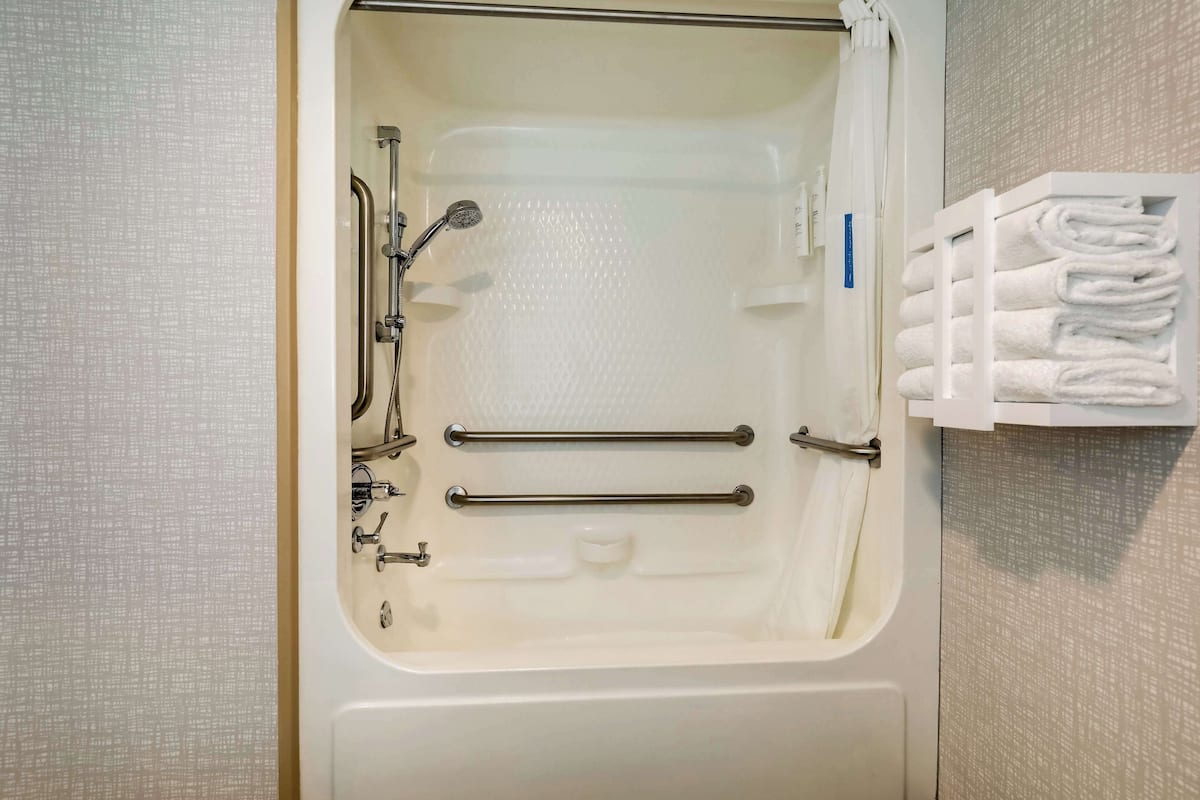 A bathroom with a bathtub, grab bars, and a towel rack.