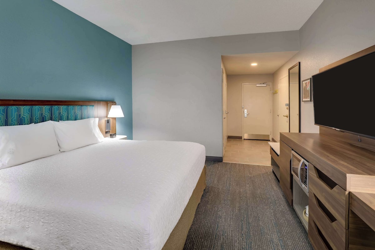 A hotel room with a large bed, a TV, a desk, and a door leading to a bathroom.