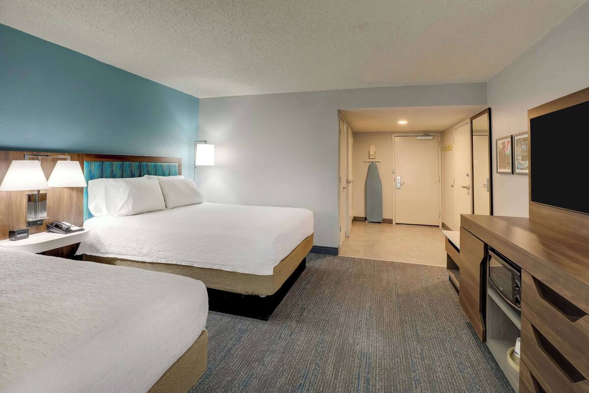 A hotel room with two beds, a desk with a lamp, a TV, and a wardrobe.