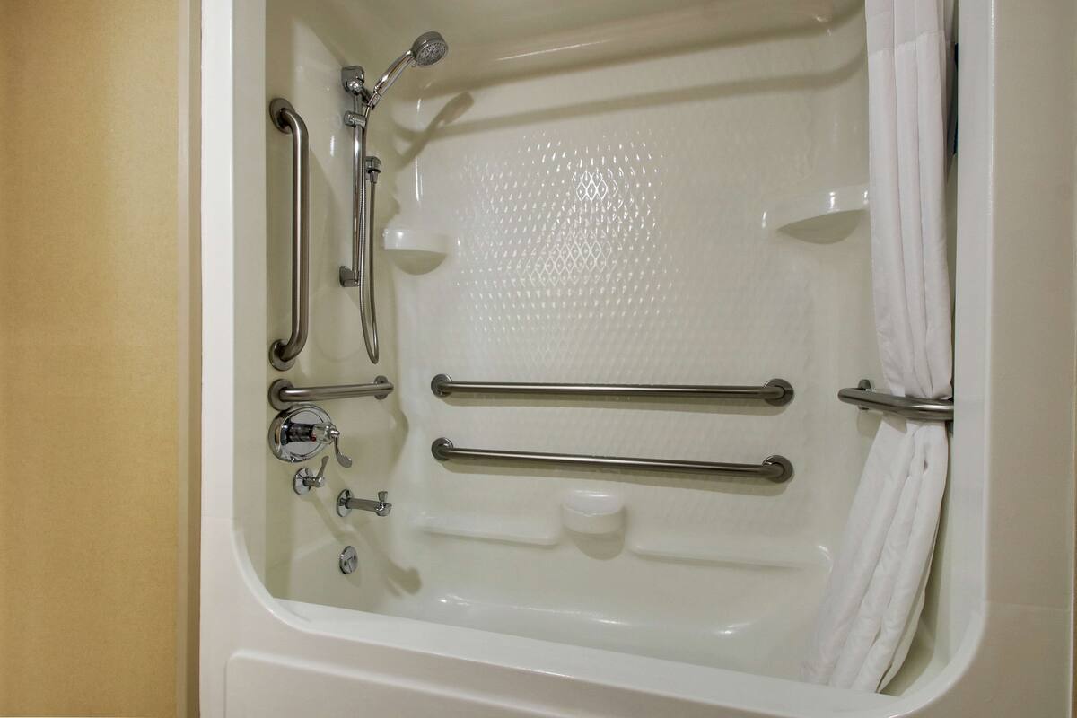 A bathtub with grab bars, a handheld showerhead, and a handheld faucet.