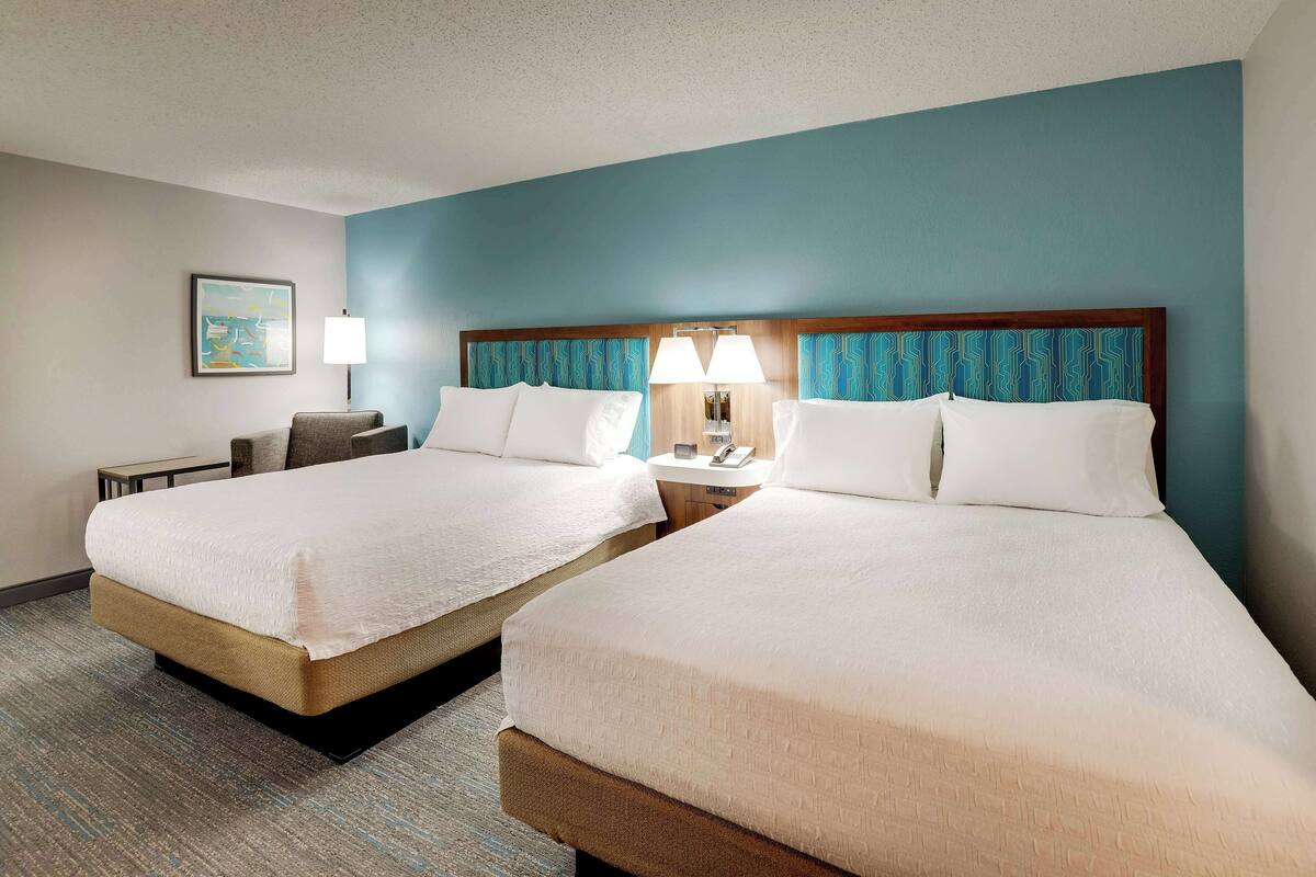 A hotel room with two beds, a nightstand, a lamp, and a framed picture on the wall.