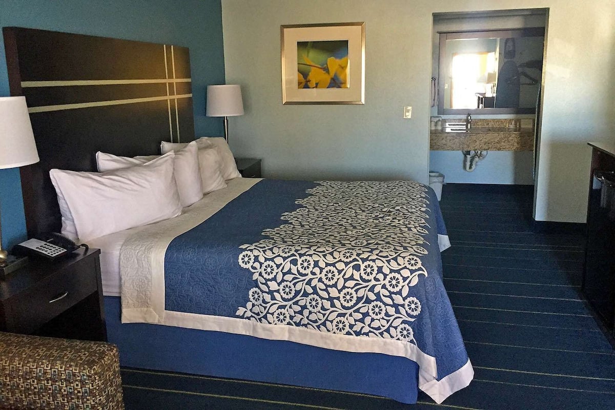 A hotel room with a bed, bedside tables, a painting, a bathroom with a sink and mirror.