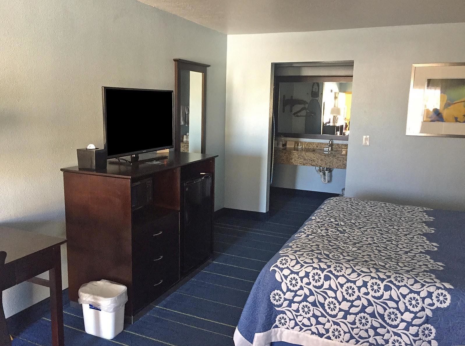 Habitación de hotel con cama, escritorio con televisor, cómoda y baño visible a través de una puerta abierta.