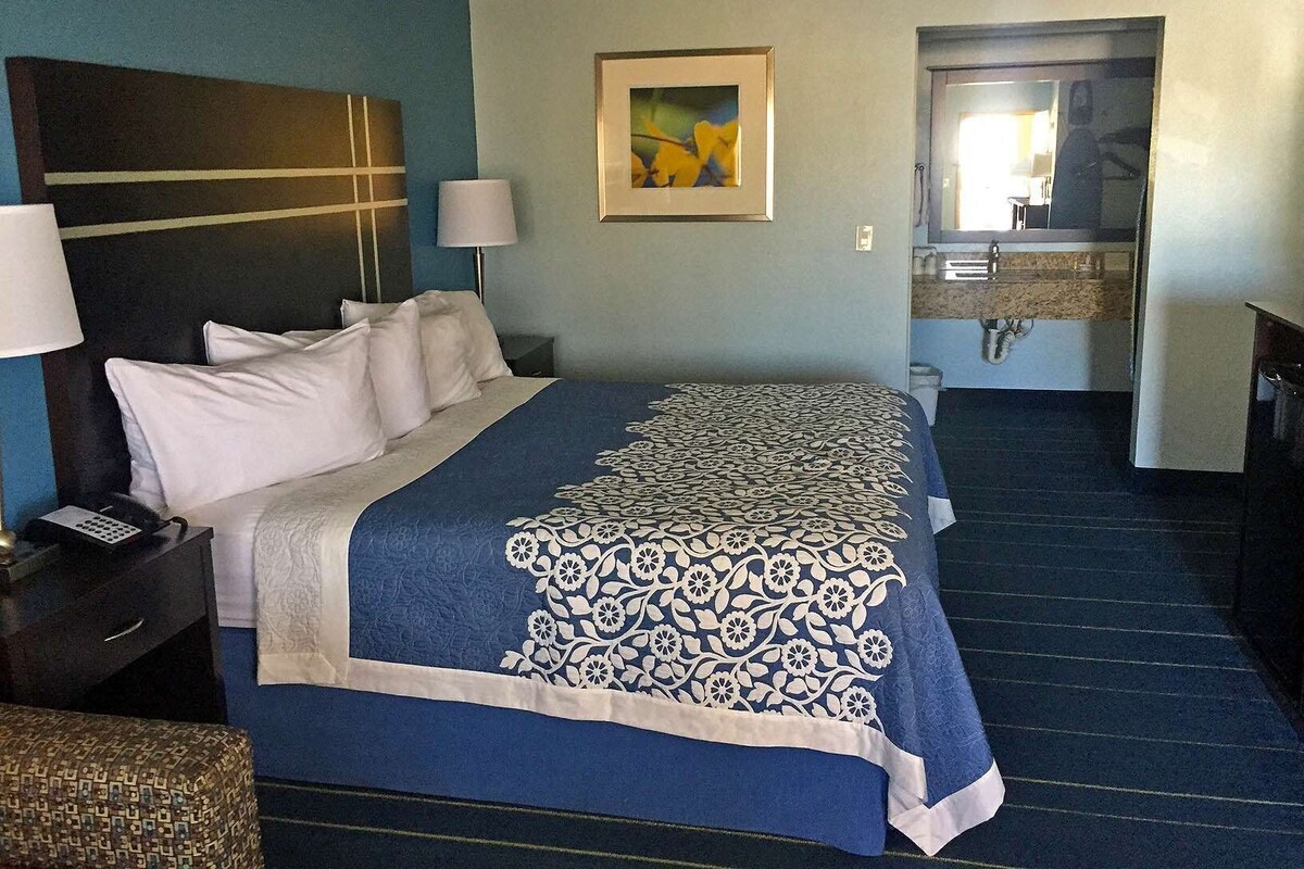 A hotel room with a bed, bedside tables, a painting, a bathroom with a sink and mirror.