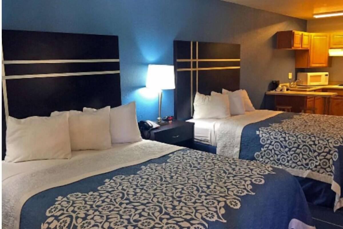 A hotel room with two beds, a desk, a lamp, and a kitchenette.