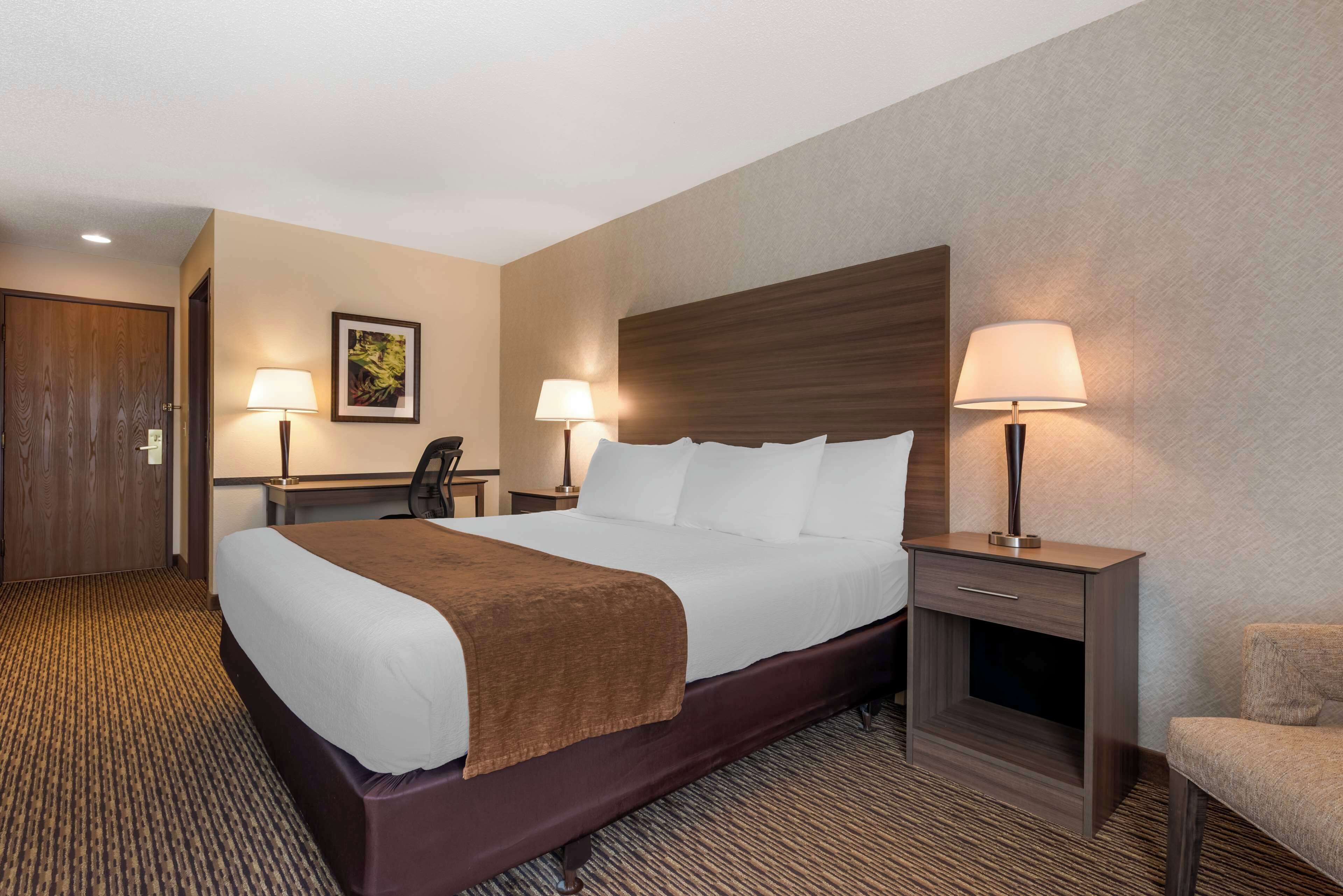 Een hotelkamer met een groot bed, twee nachtkastjes met lampen, een bureau en een stoel.