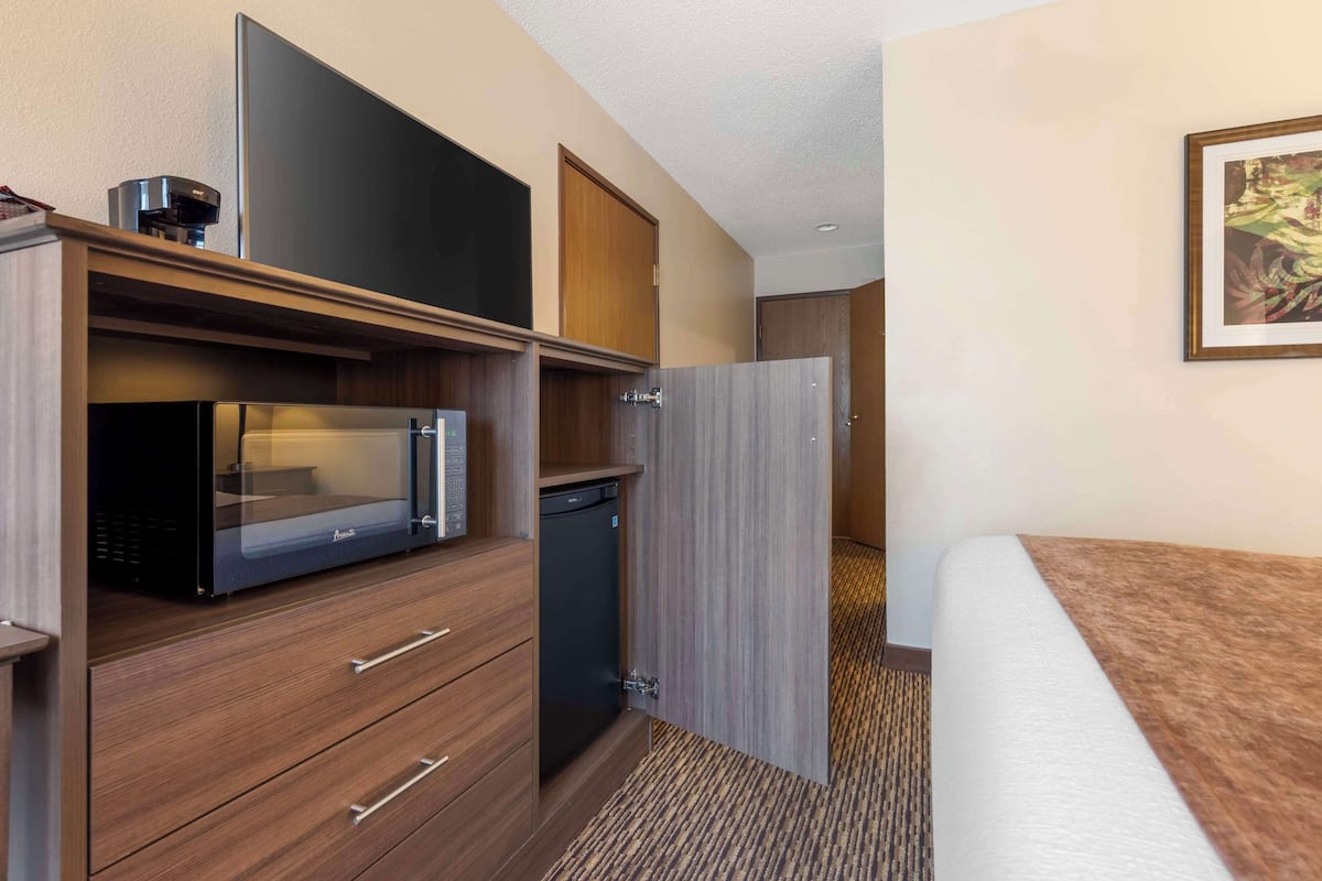 A hotel room with a bed, a microwave, a coffee maker, a mini-fridge, and a door leading to another room.