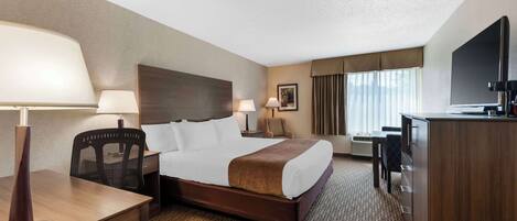 Een hotelkamer met een bed, nachtkastjes, een bureau, een stoel, een televisie en een groot raam met gordijnen.
