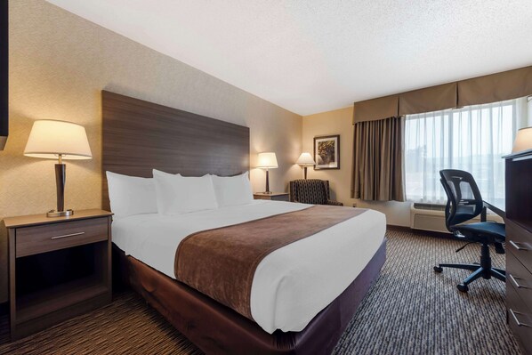 Una habitación de hotel con una cama grande, dos mesitas de noche con lámparas, un escritorio con silla y un amplio ventanal con cortinas.