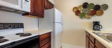 A kitchen with a stove, microwave, refrigerator, wooden cabinets, and a decorative wall plate.