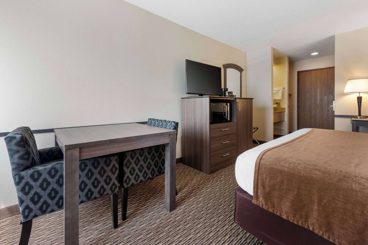 A hotel room with a bed, a desk with a chair, a television, a dresser, and a lamp.