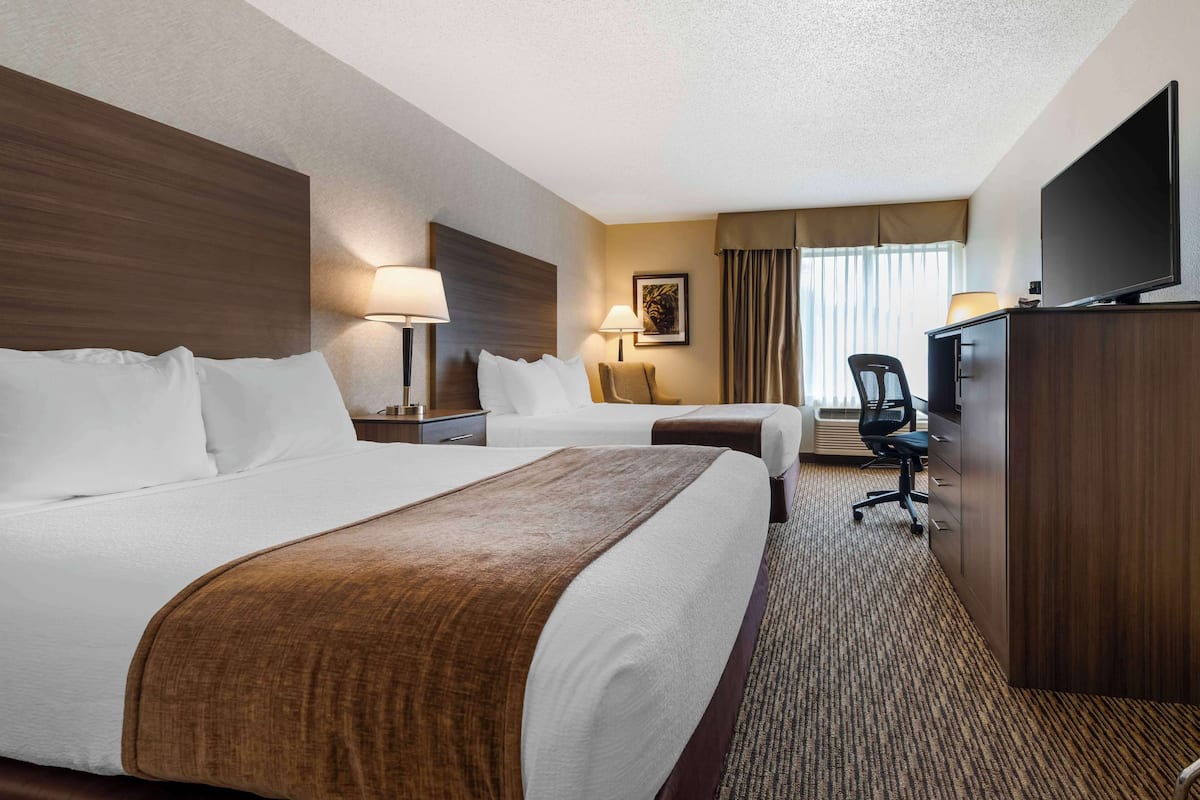 Une chambre d’hôtel avec deux lits, un bureau, une chaise, une télévision et une lampe.