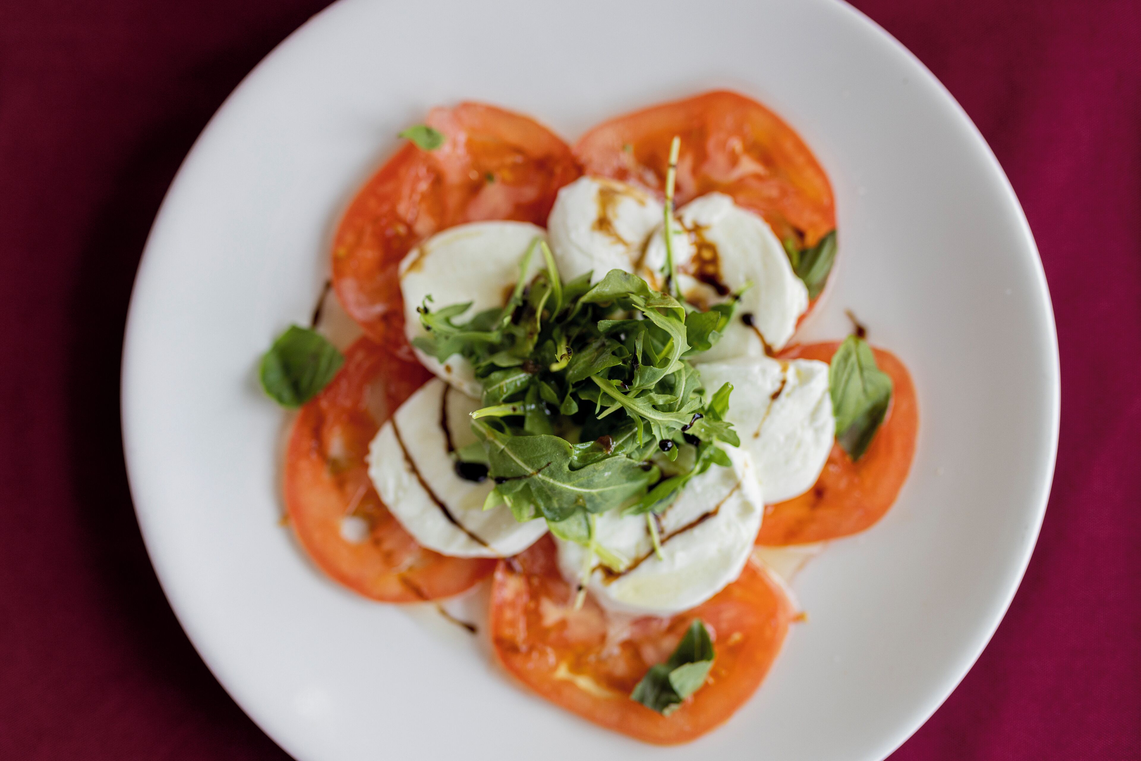 Un plato de ensalada Caprese con tomates, mozzarella y rúcula sobre un plato blanco.