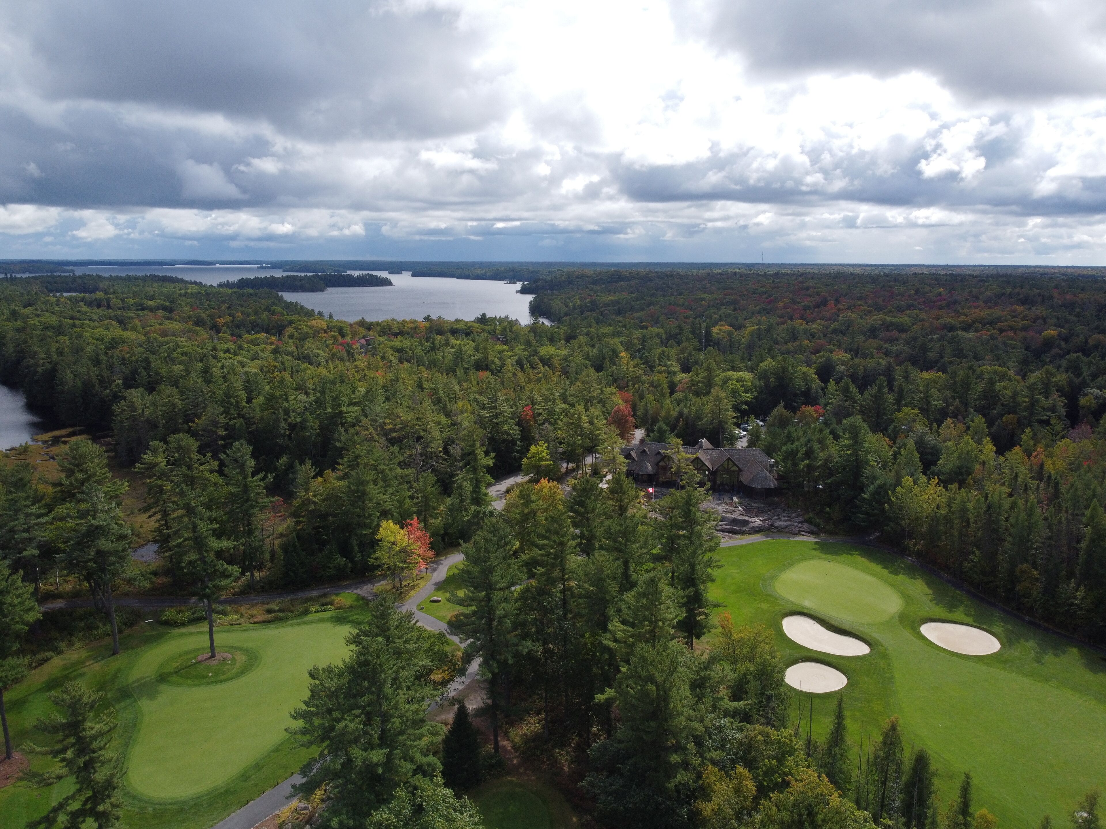 Un campo da golf con un club house, circondato da una fitta foresta e un lago sullo sfondo.