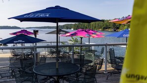 An outdoor deck with tables and chairs, umbrellas, and a view of the water. - Rocky Crest Golf Resort (Seguin)