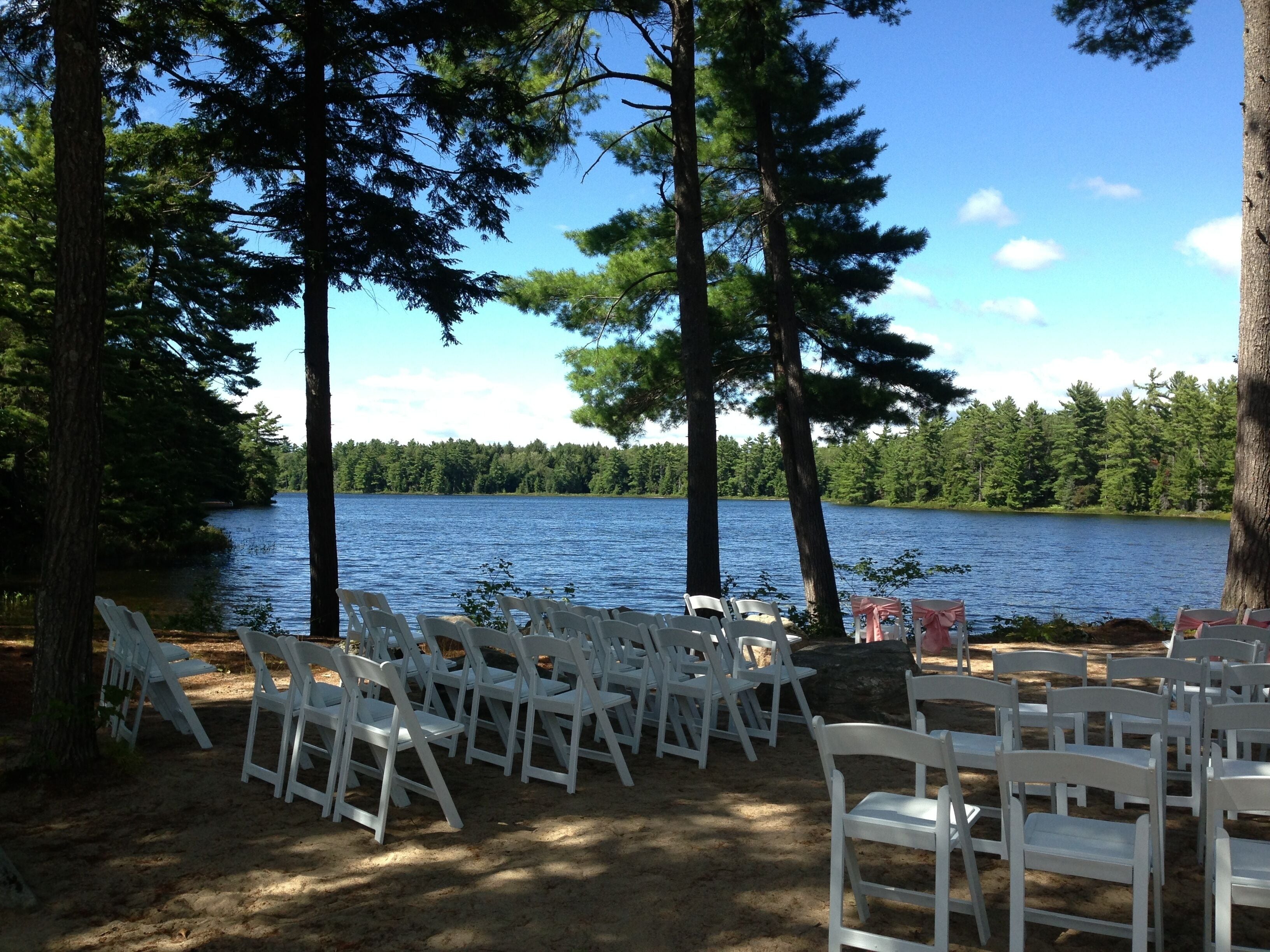 Outdoor seating arranged in rows facing a lake, surrounded by trees.