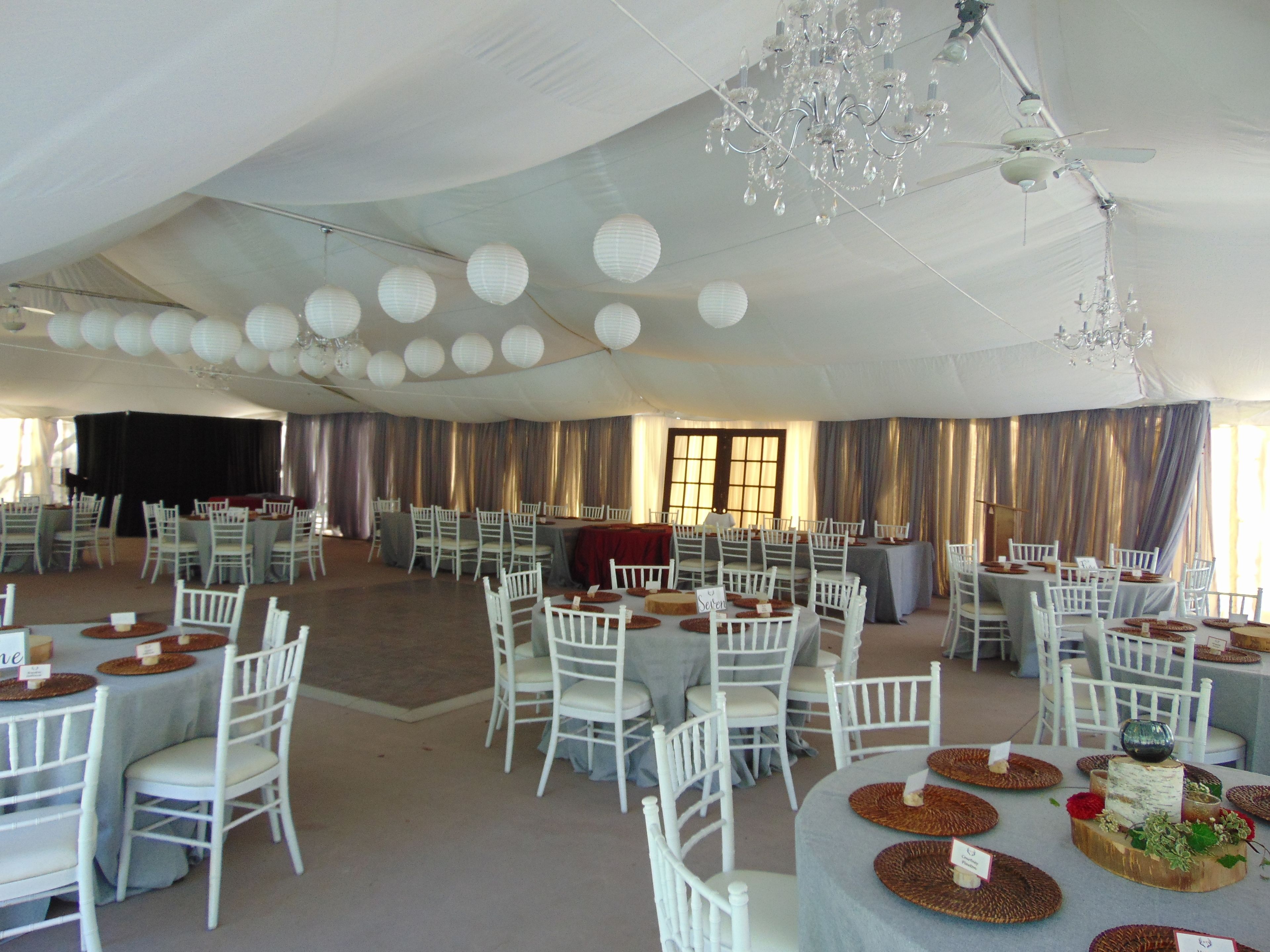 A tented event space with round tables, white chairs, and a stage area.