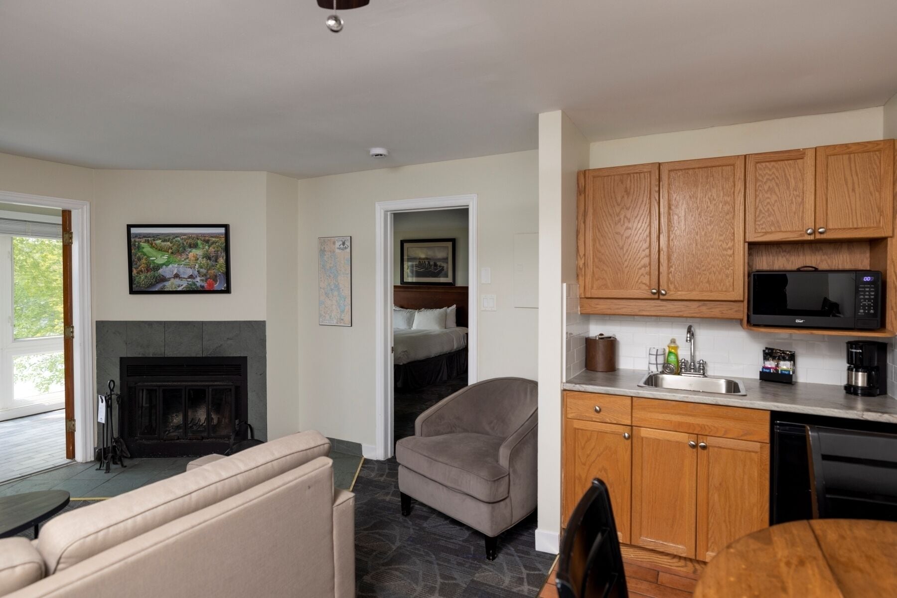 A modern kitchen with wooden cabinets, a microwave, and a coffee maker. There is a fireplace, a sofa, and a dining table.
