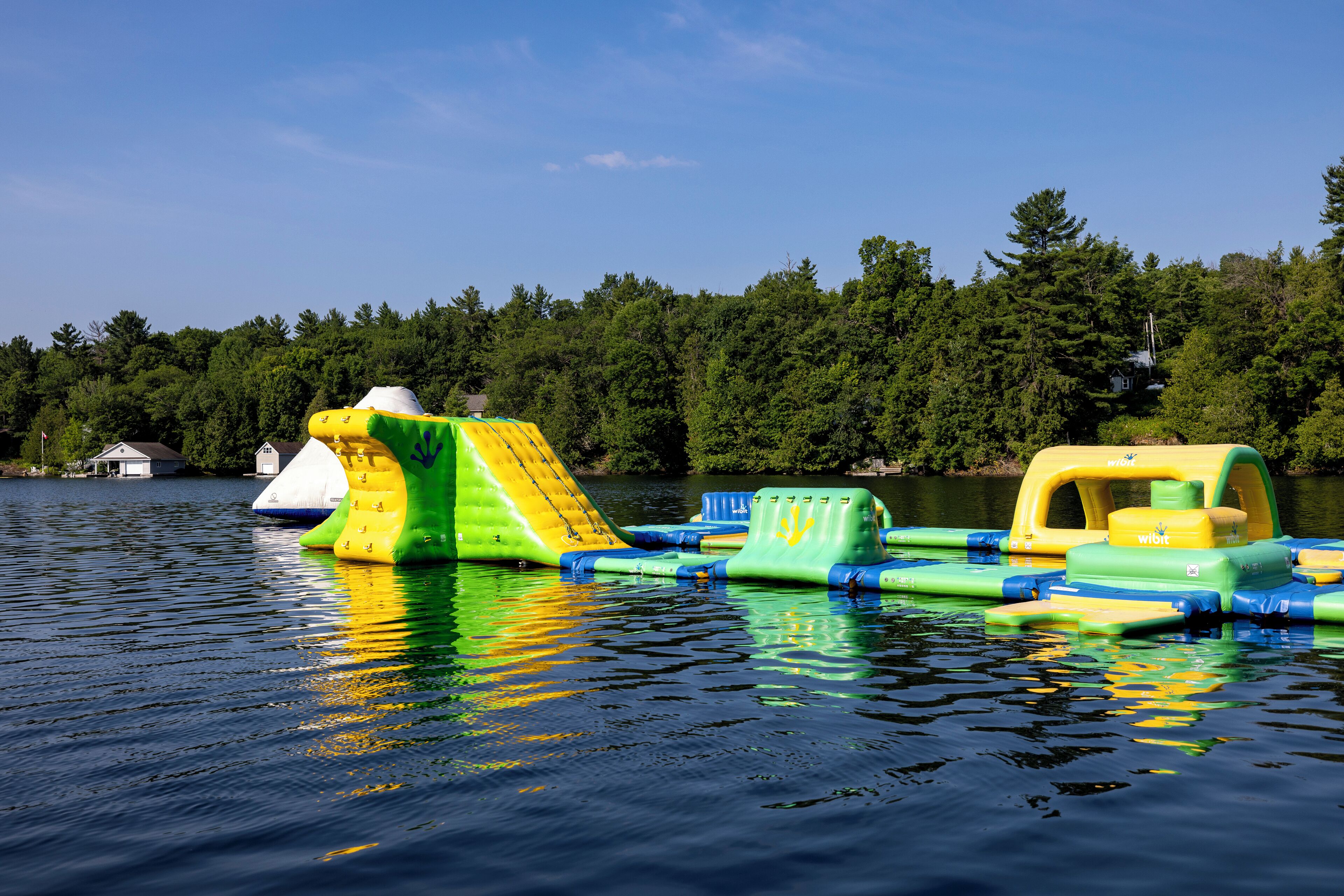 Auf einem See treiben aufblasbare Wasserrutschen und Rafting-Boote, das Ufer gesäumt von Bäumen.