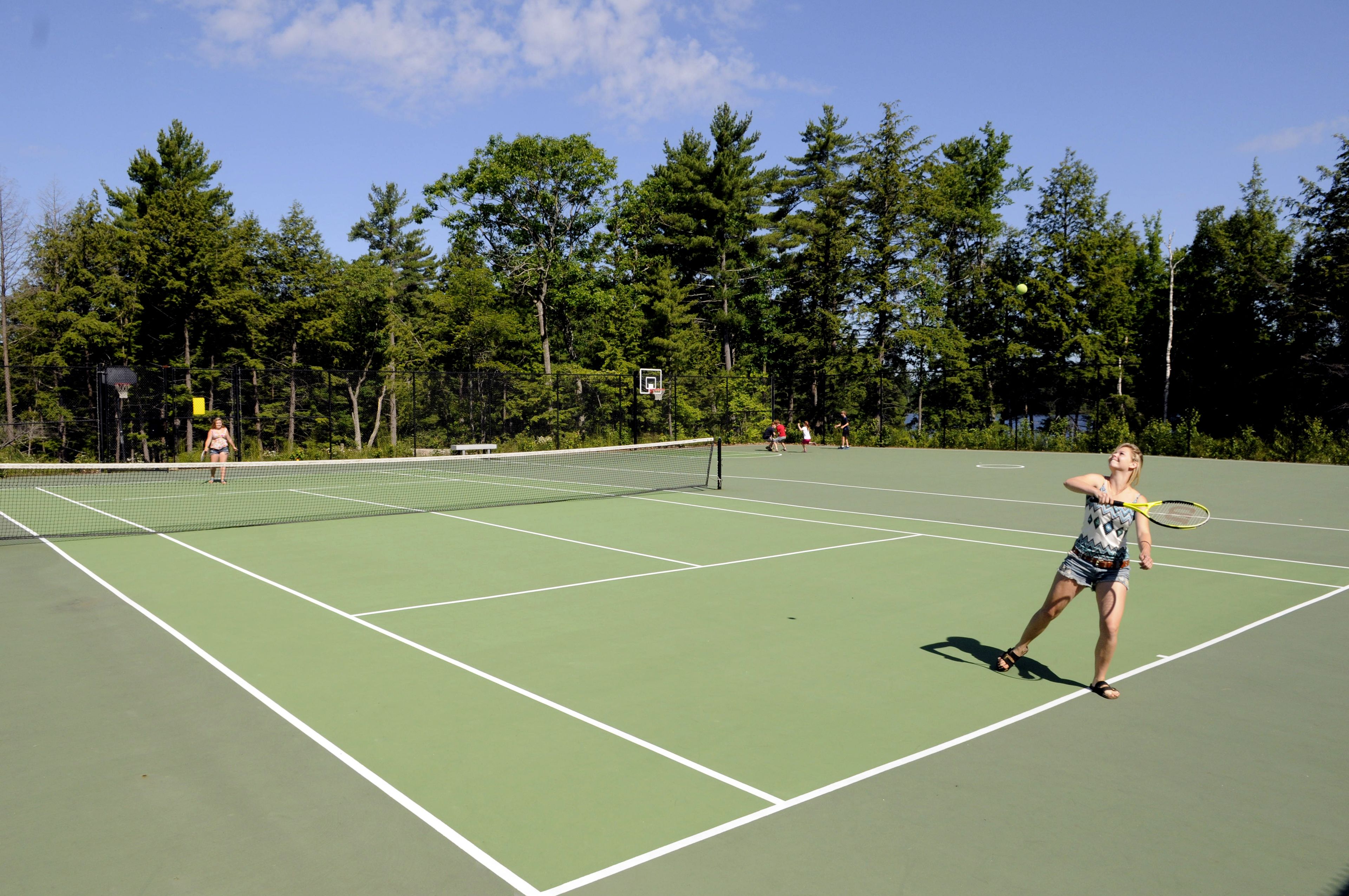 A tennis court with a net, surrounded by trees.