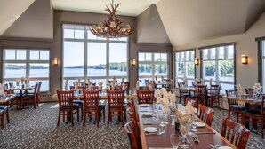 A dining area with large windows, wooden tables, and chairs, overlooking a body of water. - Rocky Crest Golf Resort (Seguin)