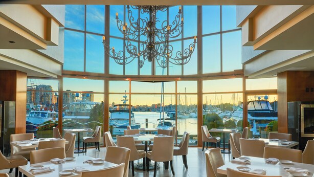 Restaurante com vista para barcos e um porto. Mesas montadas com toalhas brancas e cadeiras.