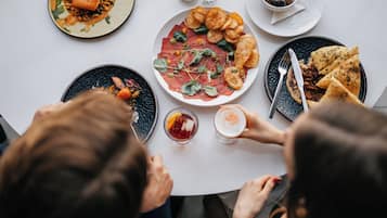 Una mesa de comedor con varios platos, entre ellos una porción de comida, un cuenco de aceitunas y un vaso de bebida.