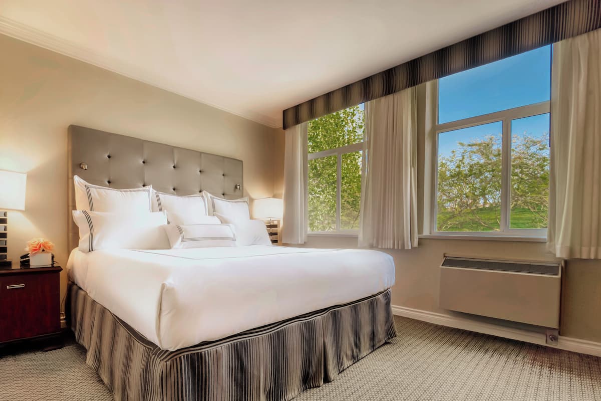 A large bed with a tufted headboard, a nightstand with a lamp, and a window with curtains.
