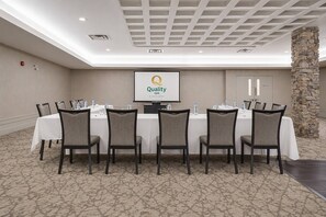 Una sala de conferencias con una pantalla grande mostrando el logotipo de Quality Inn, una mesa blanca con sillas y un pilar de piedra.