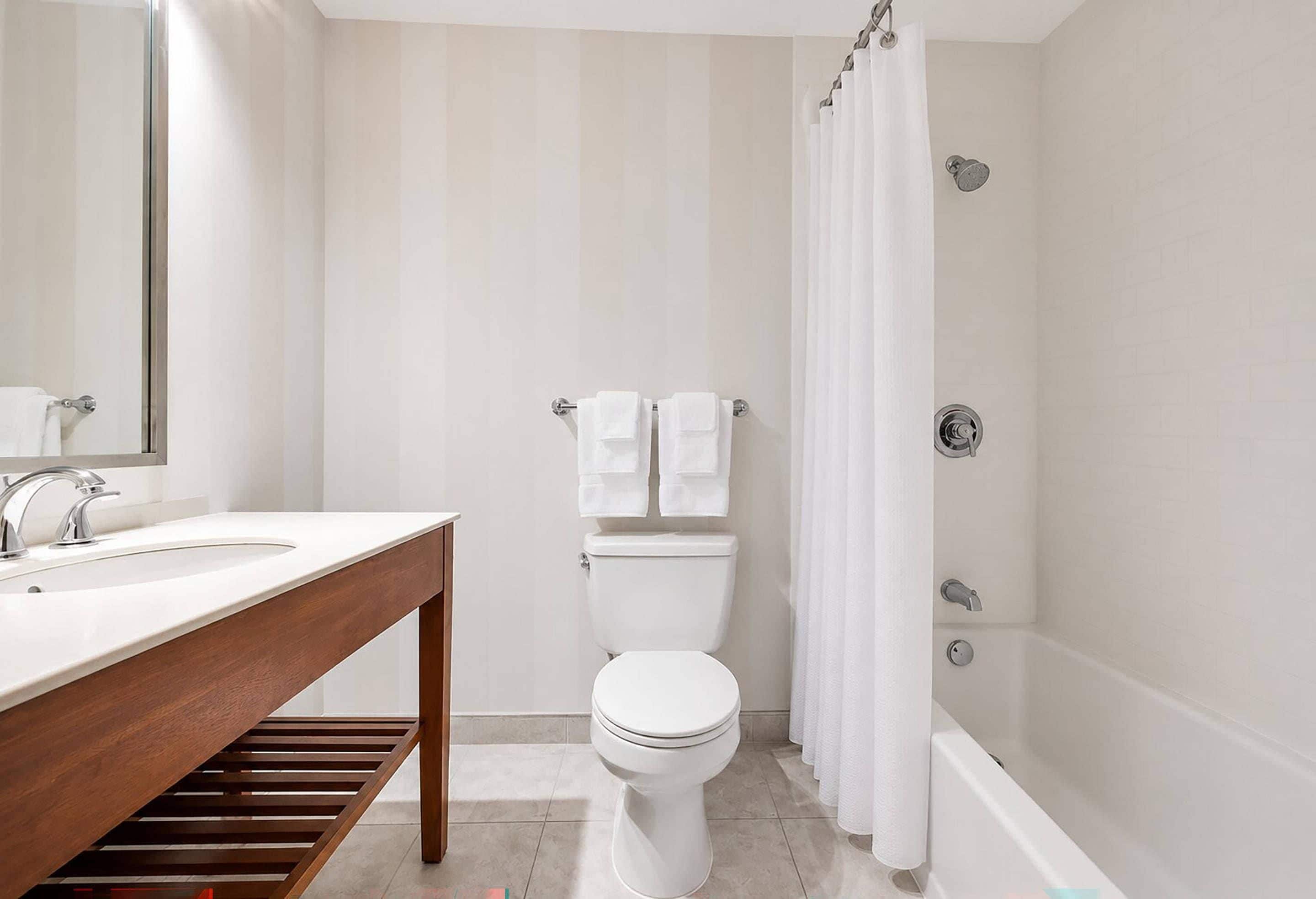A bathroom with a wooden vanity, a white toilet, and a shower with a white curtain.