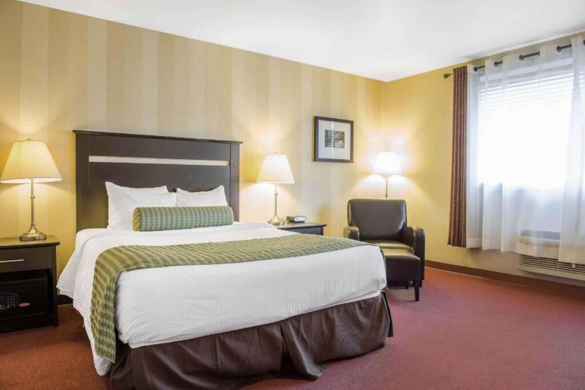 A hotel room with a bed, two bedside lamps, a chair, a picture on the wall, and a window with curtains.