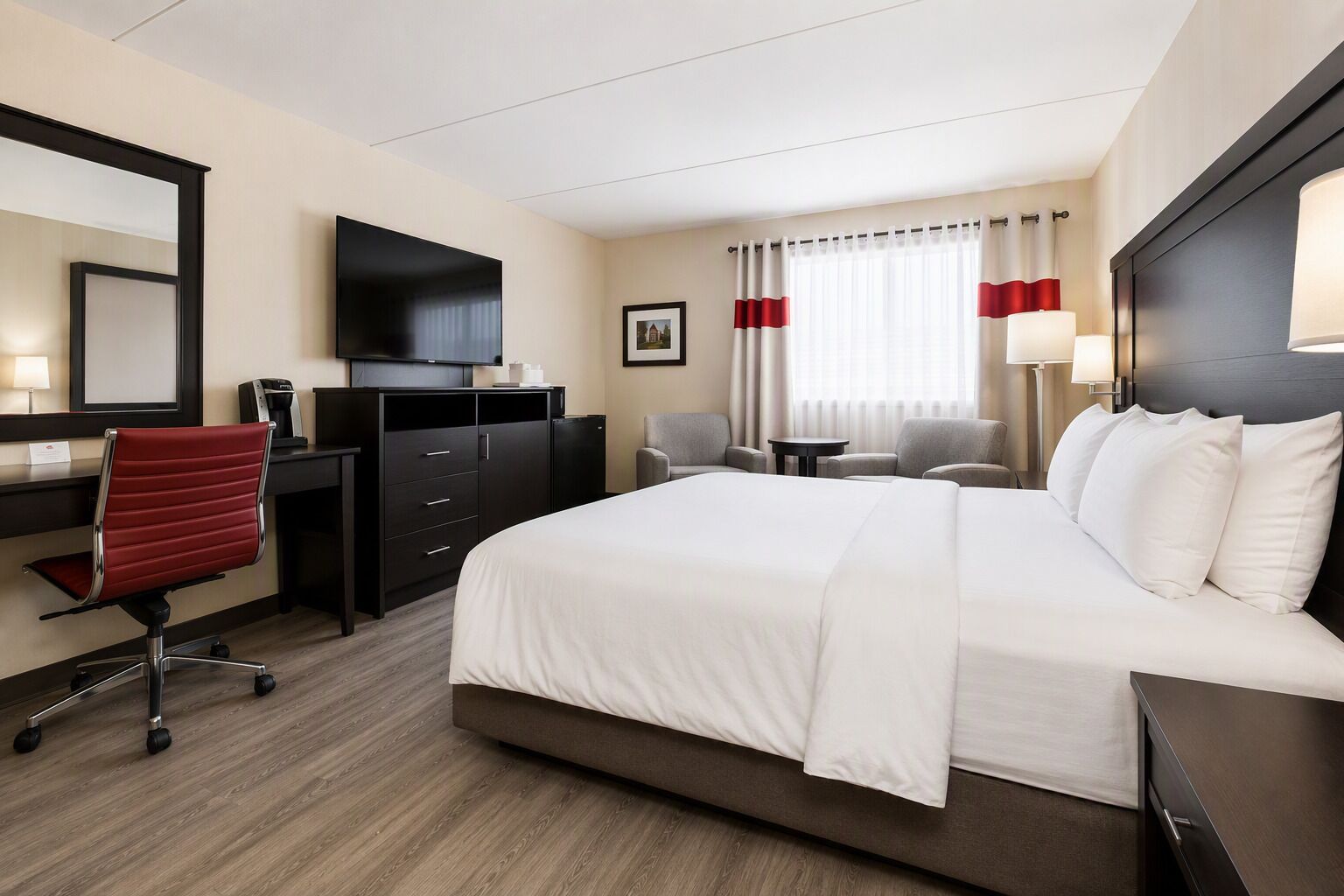 A hotel room with a large bed, a desk with a chair, a television, and a small table with two chairs.