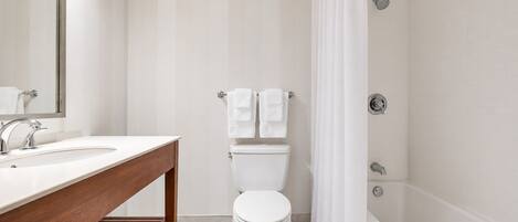 A bathroom with a wooden vanity, a toilet, a shower with a curtain, and a mirror.