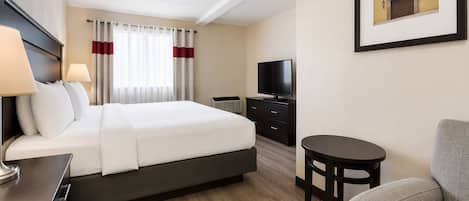 A hotel room with a bed, a desk, a chair, a television, and a framed picture on the wall.