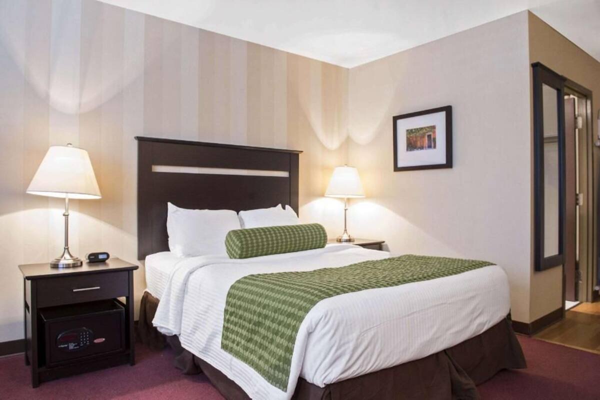 A hotel room with a bed, two bedside tables with lamps, a framed picture on the wall, and a door to the right.