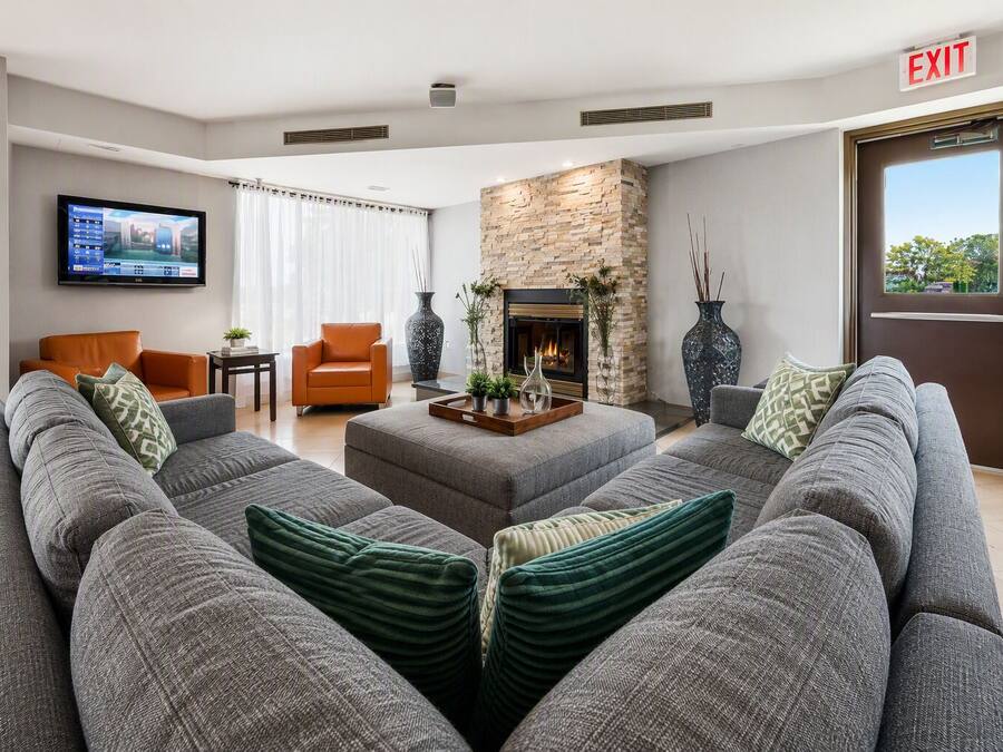 A modern living room with a large grey sofa, an orange armchair, a fireplace, and a flat-screen TV mounted on the wall.