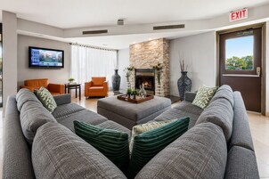 A modern living room with a large grey sofa, an orange armchair, a fireplace, and a flat-screen TV mounted on the wall.
